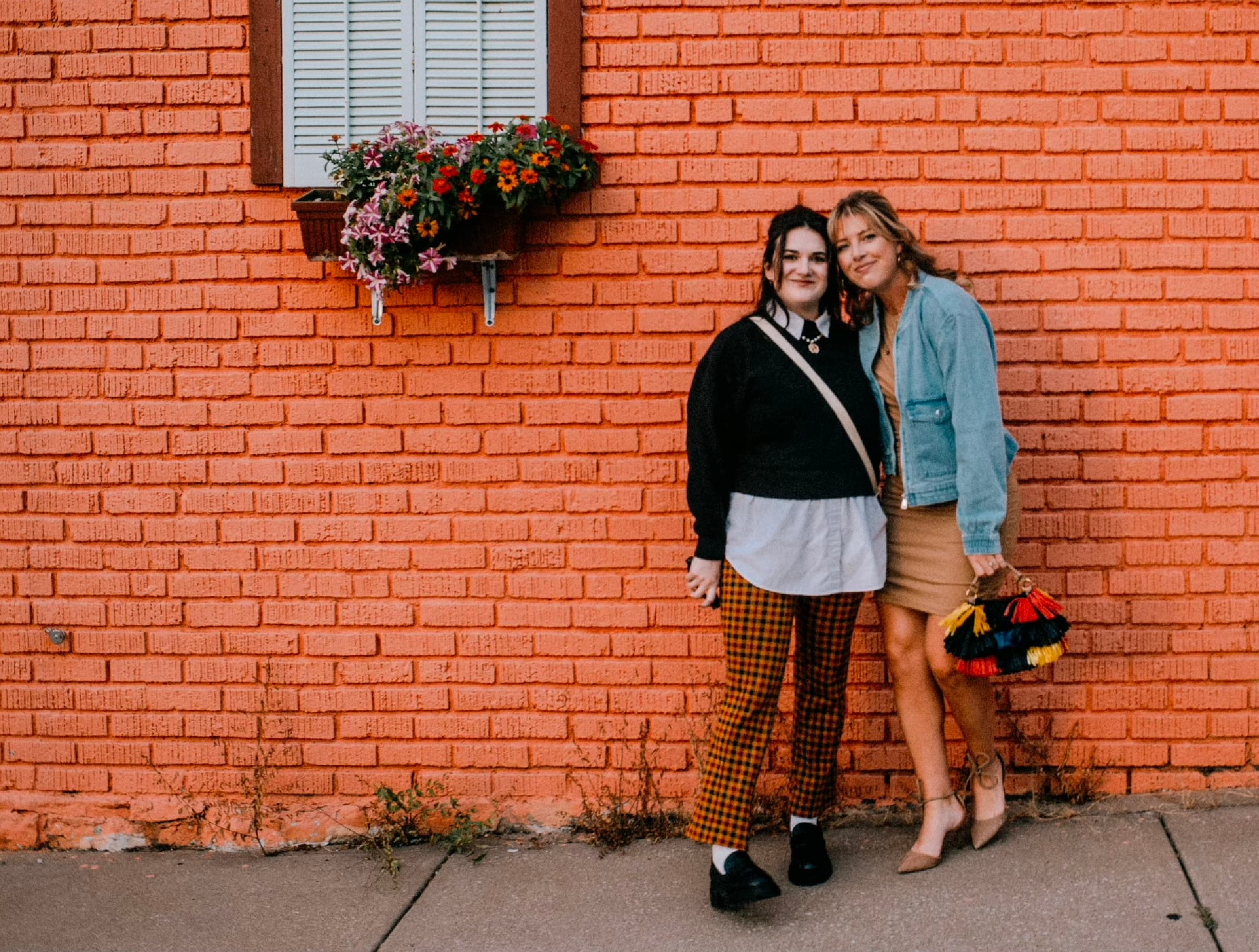 Two women standing in front of a brick wall and smiling for a photo