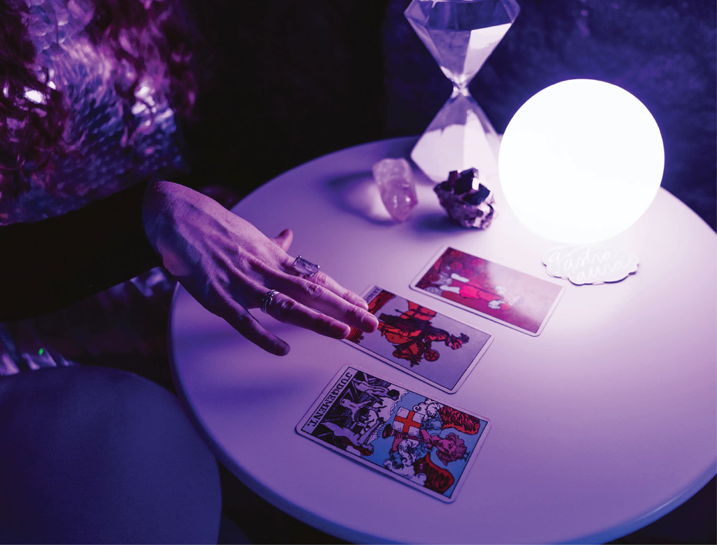A tarot card reader is showing cards on a table and there is purple light with an hour glass