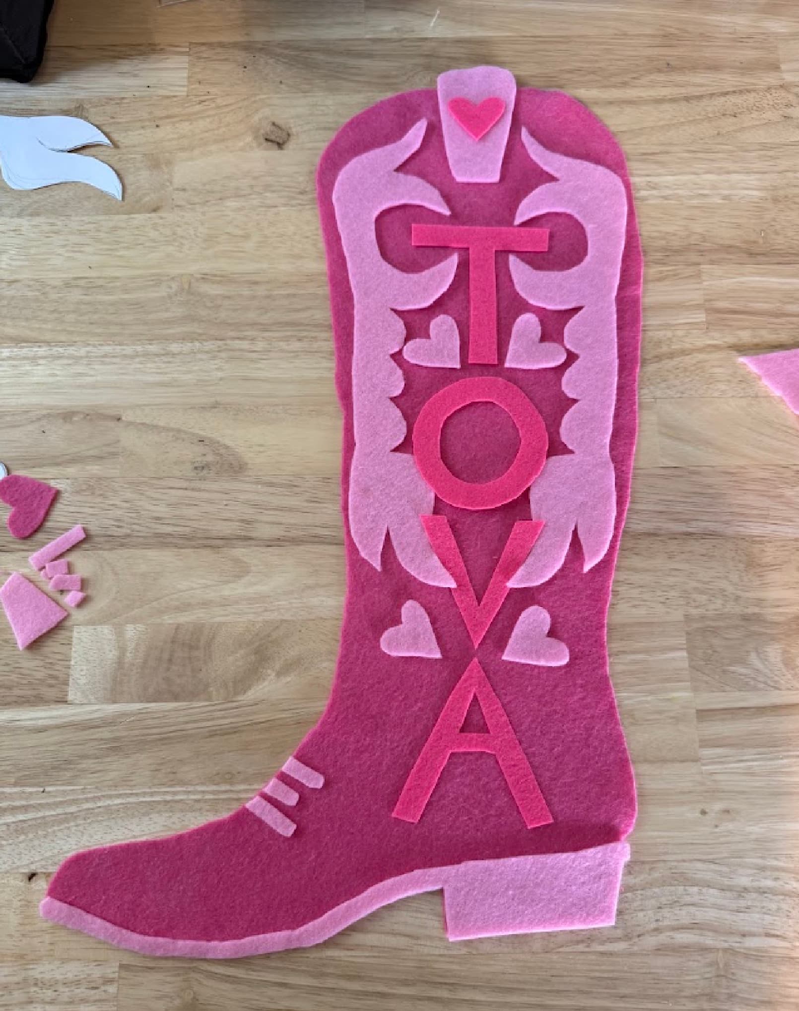 A pink, felt cowboy boot that is handmade and crafted with the letters TOVA